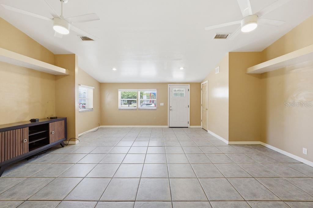 A spacious living room features light-colored tile flooring, beige walls, two ceiling fans, and built-in shelving — 7207 S WEST SHORE BOULEVARD, TAMPA, FL