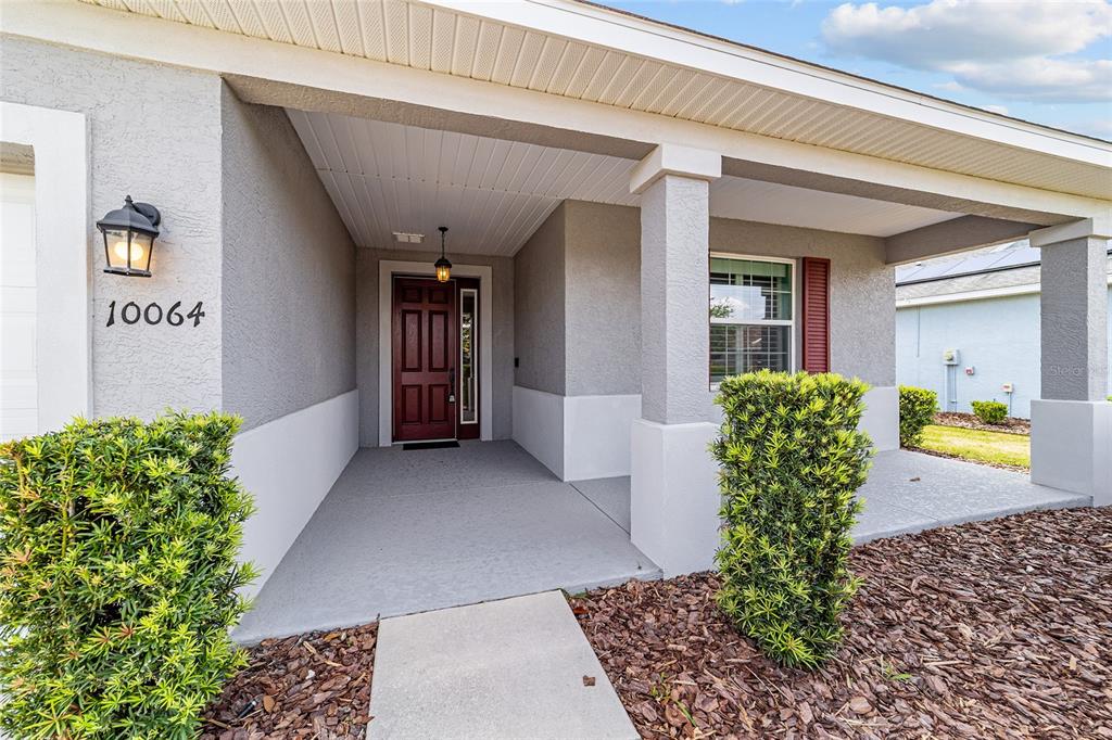 A covered front porch leads to a dark red front door with a side window — 10064 SW 88TH STREET, OCALA, FL