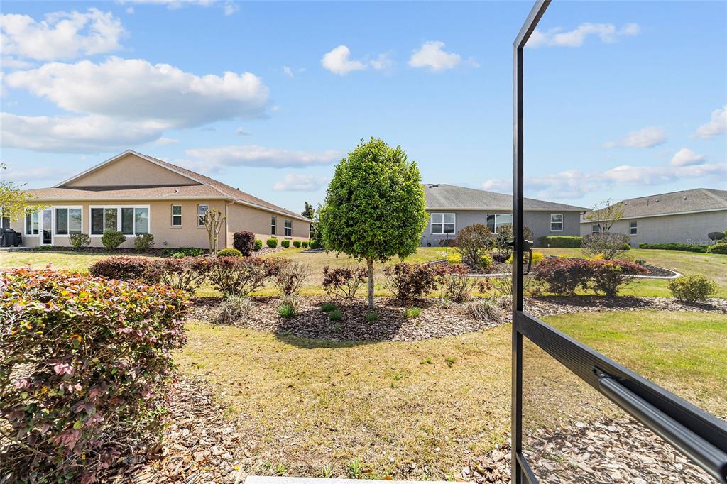 A view of a backyard with a central tree, landscaping, and neighboring houses — 10064 SW 88TH STREET, OCALA, FL