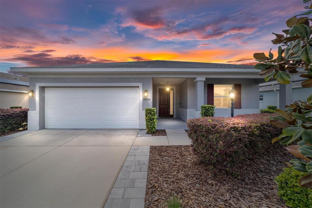 A single-story house with a two-car garage and a landscaped front yard at sunset — 10064 SW 88TH STREET, OCALA, FL