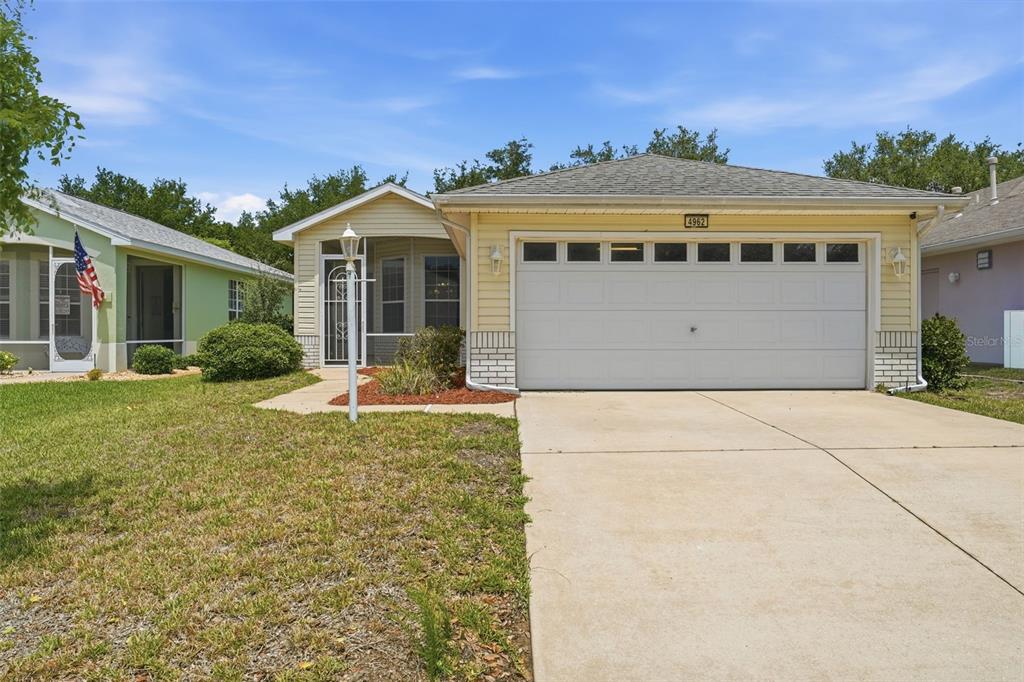 A single-story house with yellow siding, a white garage door, and a screened front entryway — 4962 RAINBOW TROUT ROAD, TAVARES, FL