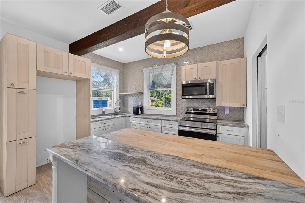 A kitchen features light wood cabinets, a stone-topped island, and a wooden ceiling beam — 1121 SE 29TH STREET, OCALA, FL