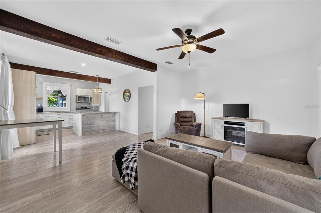 An open-concept living room and kitchen feature wood-look flooring, exposed ceiling beams, and neutral walls — 1121 SE 29TH STREET, OCALA, FL