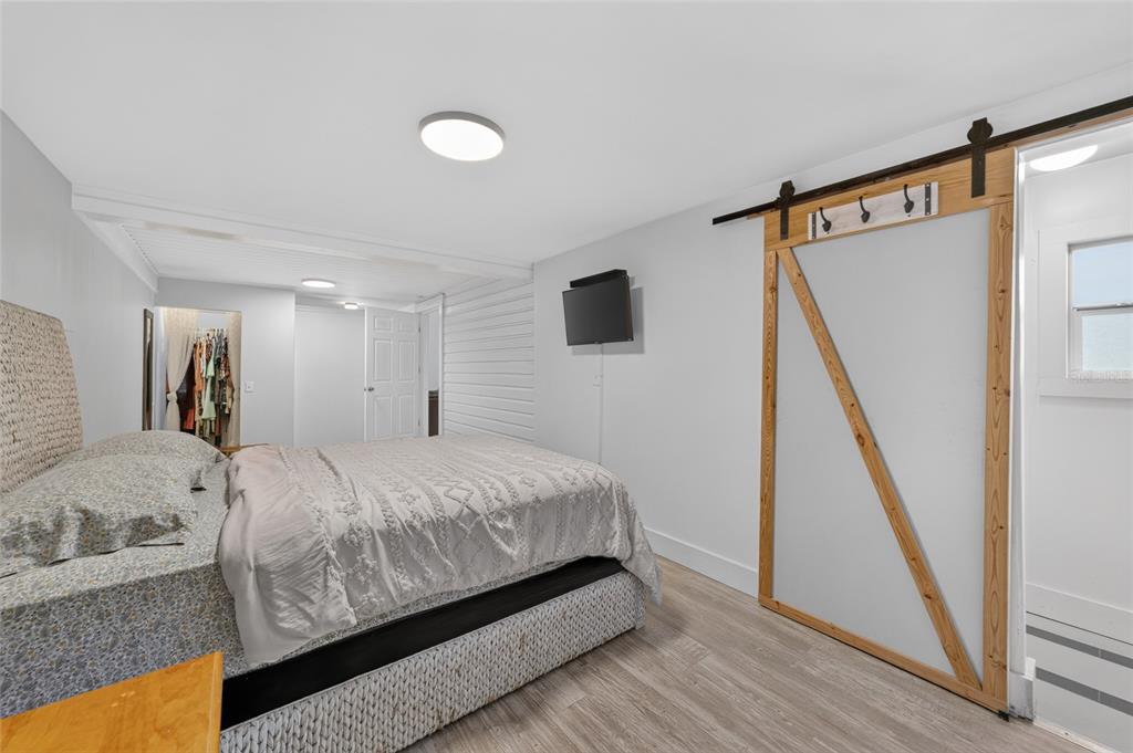 A bedroom features a bed, light wood flooring, a wall-mounted television, and a sliding barn door — 1121 SE 29TH STREET, OCALA, FL