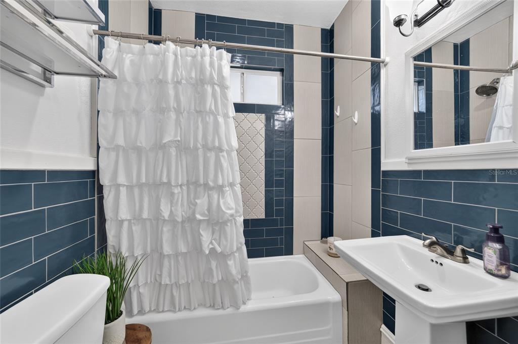 A bathroom features a white pedestal sink, a bathtub, and blue and beige tiled walls — 1121 SE 29TH STREET, OCALA, FL