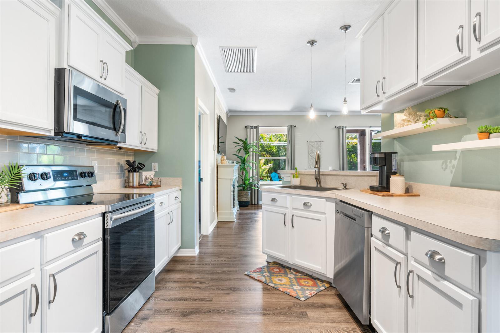 A kitchen with white cabinets, stainless steel appliances, and sage green walls opens to a living area — SEBASTIAN, FL