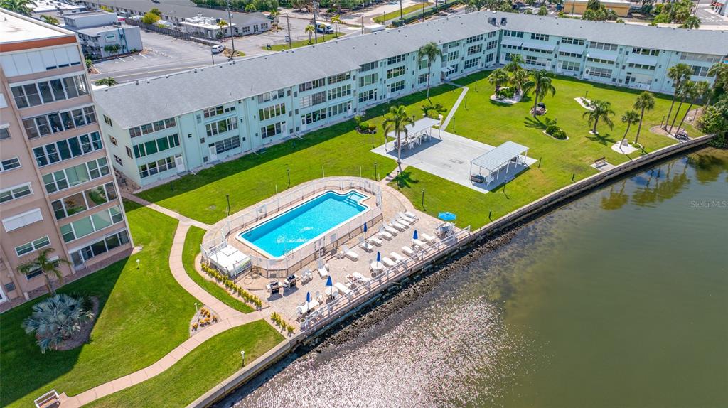 An aerial view shows a waterfront apartment complex with a swimming pool and patio area — 1847 SHORE DRIVE S UNIT 509, ST PETERSBURG, FL