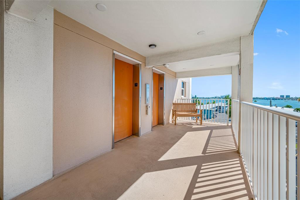 An outdoor apartment building hallway features two orange elevator doors, a wooden bench, and railings — 1847 SHORE DRIVE S UNIT 509, ST PETERSBURG, FL