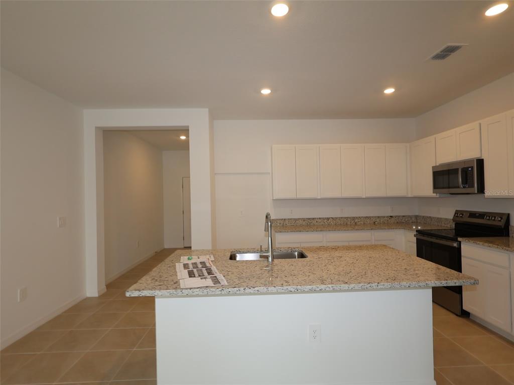 A kitchen features white cabinets, granite countertops, a central island with a sink, and appliances — 4520 OUTHAUL RUN, PALMETTO, FL