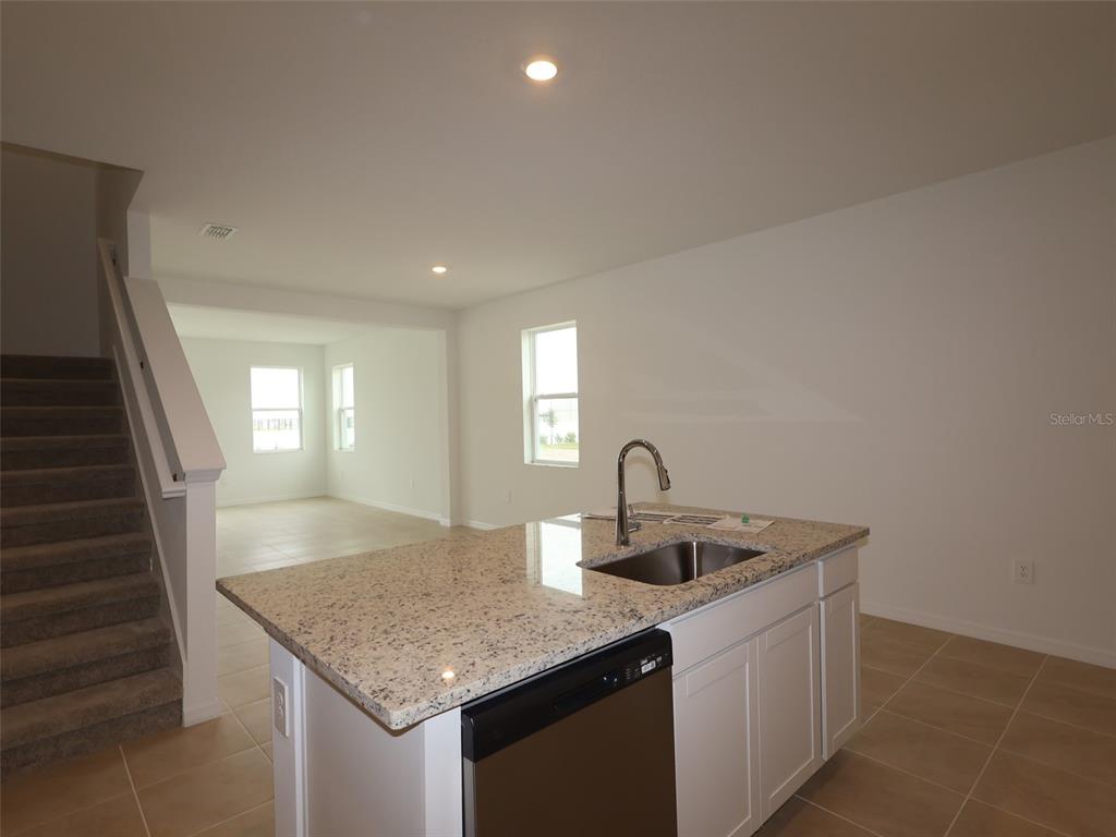 A kitchen island with a granite countertop and stainless steel sink sits before a staircase — 4520 OUTHAUL RUN, PALMETTO, FL