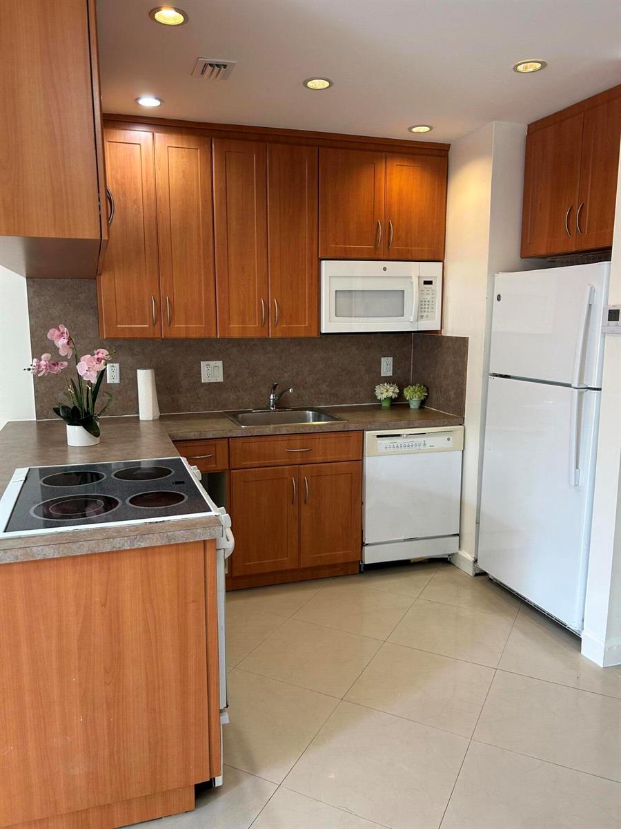 A kitchen features wood cabinets, a white refrigerator, a dishwasher, and a stovetop island — 210 SE 9th Street # 1, Hallandale Beach FL 33009, HALLANDALE BEACH, FL
