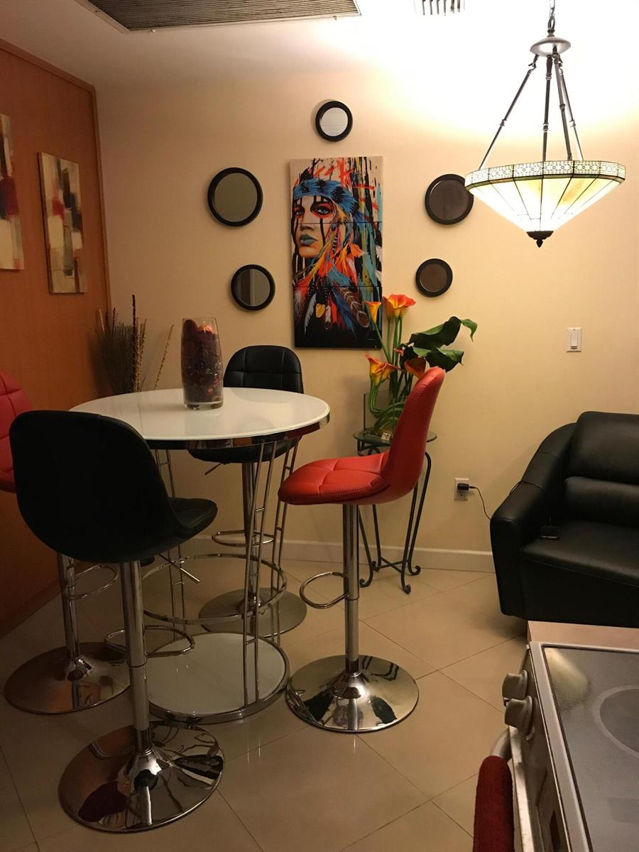 A dining area features a round white table, bar stools, and wall art — 210 SE 9th Street # 1, Hallandale Beach FL 33009, HALLANDALE BEACH, FL