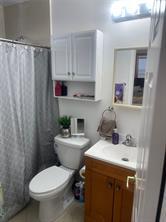 A bathroom features a white toilet, a wooden vanity with a sink, and wall-mounted cabinets — 210 SE 9th Street # 1, Hallandale Beach FL 33009, HALLANDALE BEACH, FL