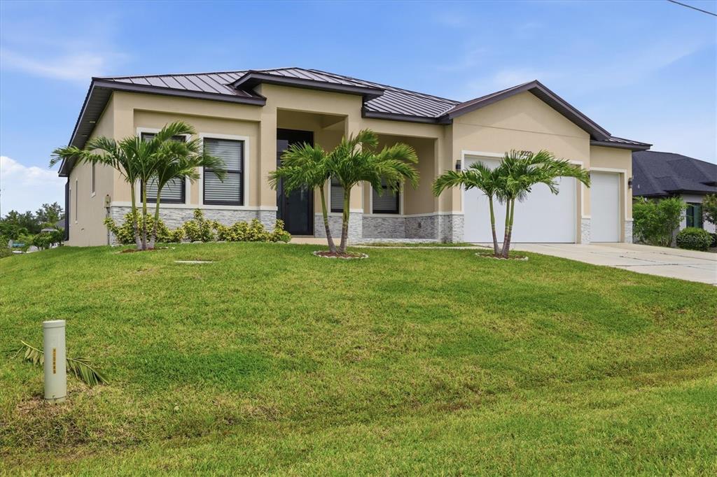 A single-story house with a tan stucco exterior, metal roof, and three palm trees — 9222 ROSEBUD CIRCLE, PORT CHARLOTTE, FL