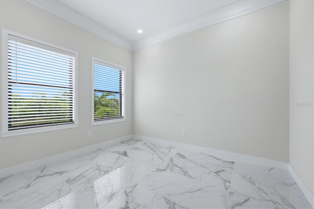 An empty room features white walls, crown molding, and polished white marble-look tile flooring — 9222 ROSEBUD CIRCLE, PORT CHARLOTTE, FL