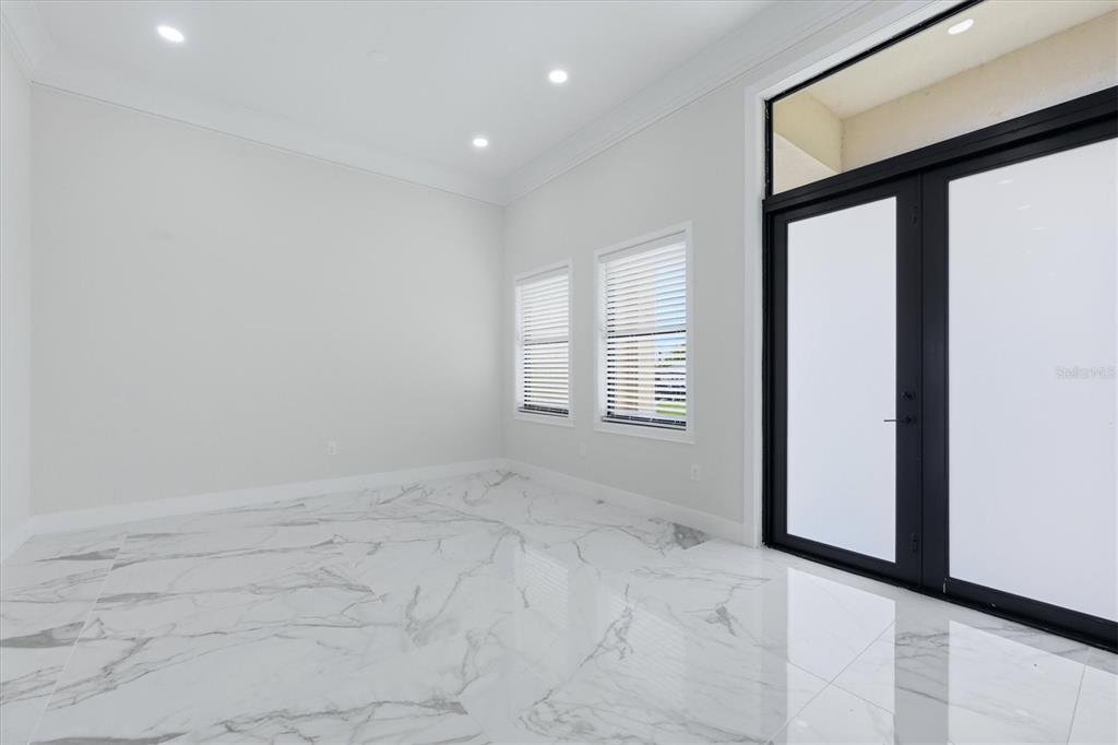 An empty room with white walls, recessed lighting, marble-look tile floors, and black-framed glass doors — 9222 ROSEBUD CIRCLE, PORT CHARLOTTE, FL