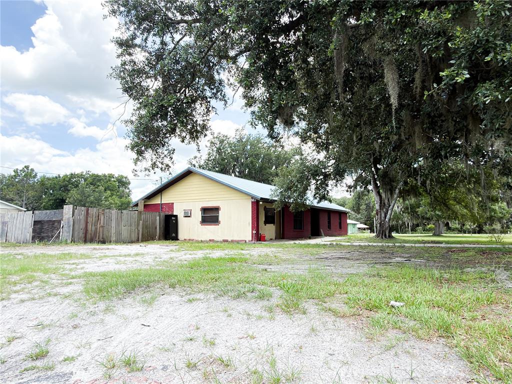 A single-story house with yellow and red siding stands behind a large, moss-draped oak tree — 415 3RD STREET W, ZOLFO SPRINGS, FL