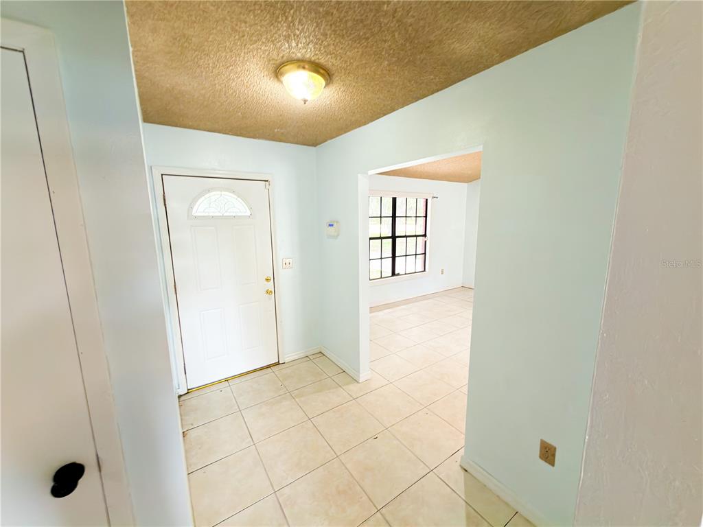 An entryway with light-colored tile flooring leads to a doorway and an adjacent living area — 415 3RD STREET W, ZOLFO SPRINGS, FL