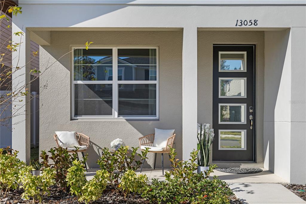 A front porch features two wicker chairs, a small table, and a modern dark door — 13058 PERGOLA AVENUE, ORLANDO, FL