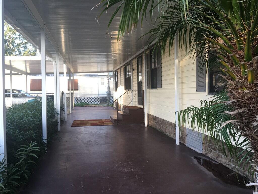 A covered concrete patio runs alongside a light-yellow mobile home with dark brown steps — 1163 20th Street, Okeechobee FL 34974, OKEECHOBEE, FL