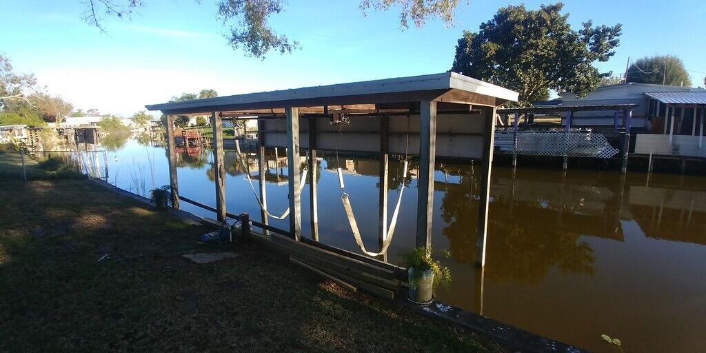 A boat lift with a metal roof stands over a canal next to a grassy yard — 1163 20th Street, Okeechobee FL 34974, OKEECHOBEE, FL