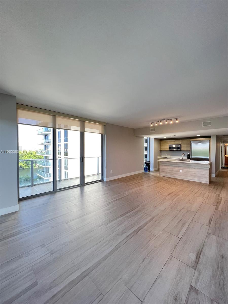 An open-concept living area features light wood-look tile flooring, a kitchen island, and balcony access — 16385 Biscayne Blvd # 607, North Miami Beach FL 33160, NORTH MIAMI BEACH, FL