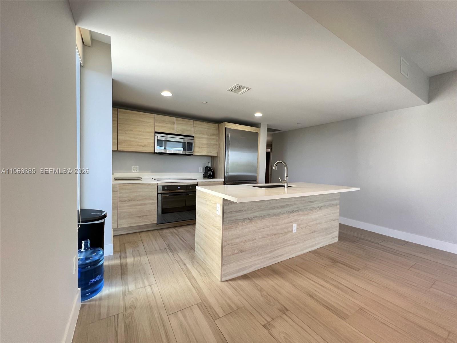 A modern kitchen features light wood cabinets, stainless steel appliances, and a central island — 16385 Biscayne Blvd # 607, North Miami Beach FL 33160, NORTH MIAMI BEACH, FL