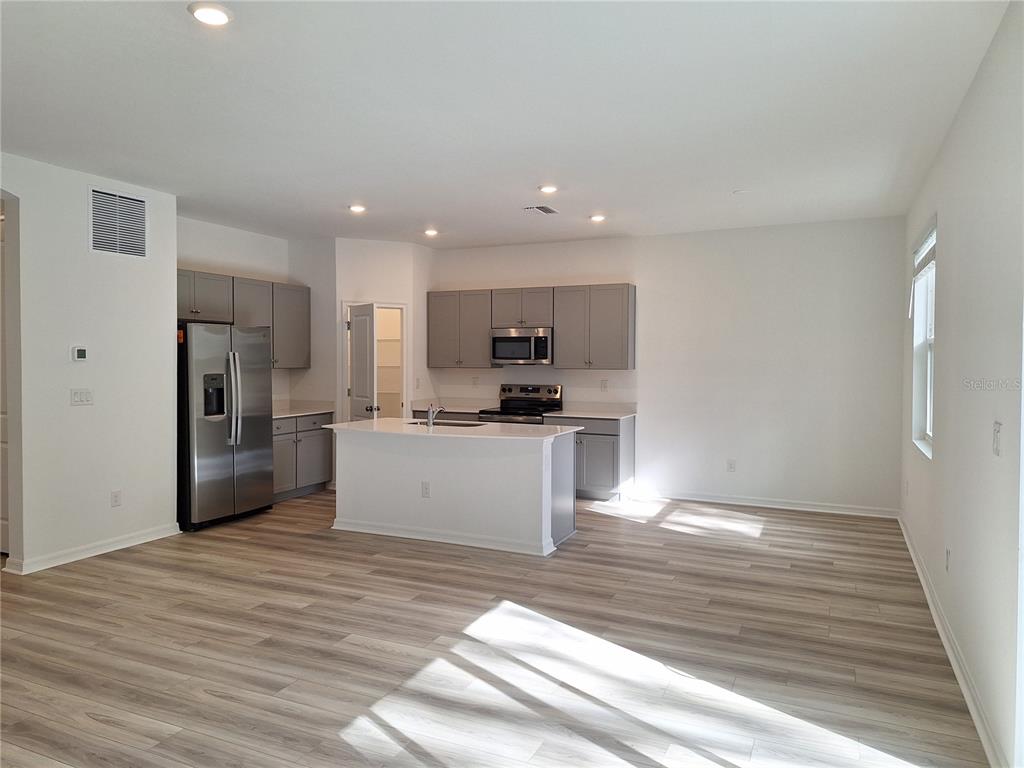 A modern kitchen features gray cabinets, stainless steel appliances, a white island, and wood-look flooring — 34916 MULRION DRIVE, ZEPHYRHILLS, FL