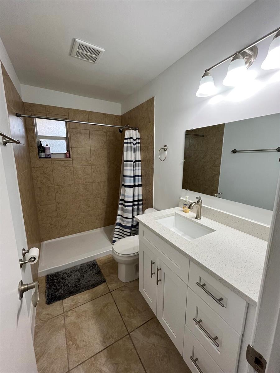 A bathroom features a white vanity, a tiled shower stall, and beige floor tiles — 1979 Juno Road, North Palm Beach FL 33408, NORTH PALM BEACH, FL