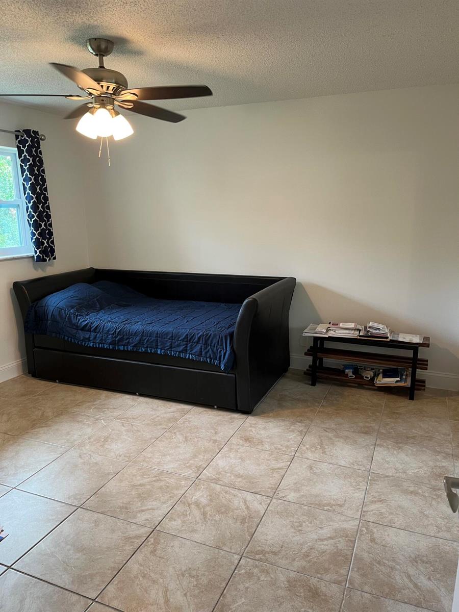 A bedroom with a black daybed, a small wooden shelf, and tile flooring — 1979 Juno Road, North Palm Beach FL 33408, NORTH PALM BEACH, FL