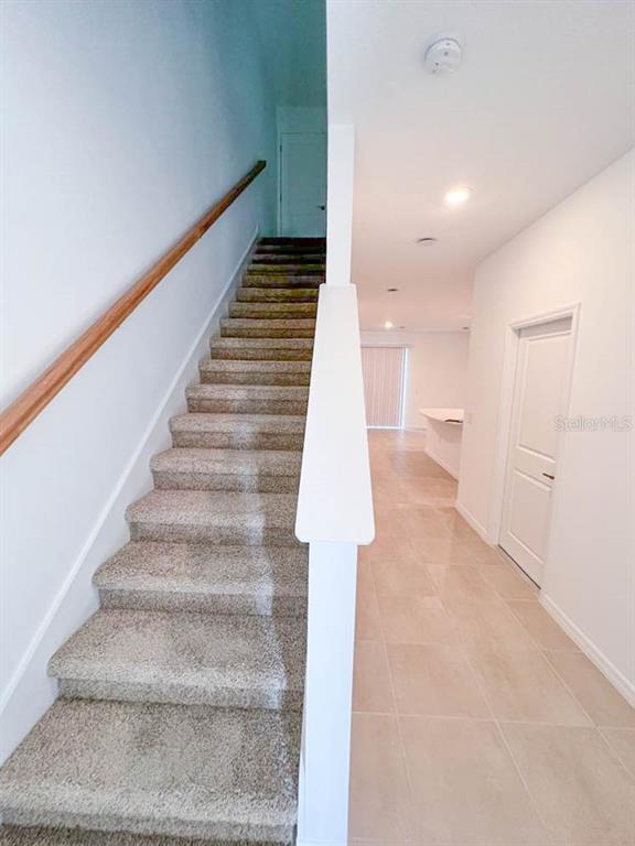 A carpeted staircase with a wooden handrail sits beside a tiled hallway leading to a kitchen — 3639 DAVENPORT CREEK COURT, KISSIMMEE, FL