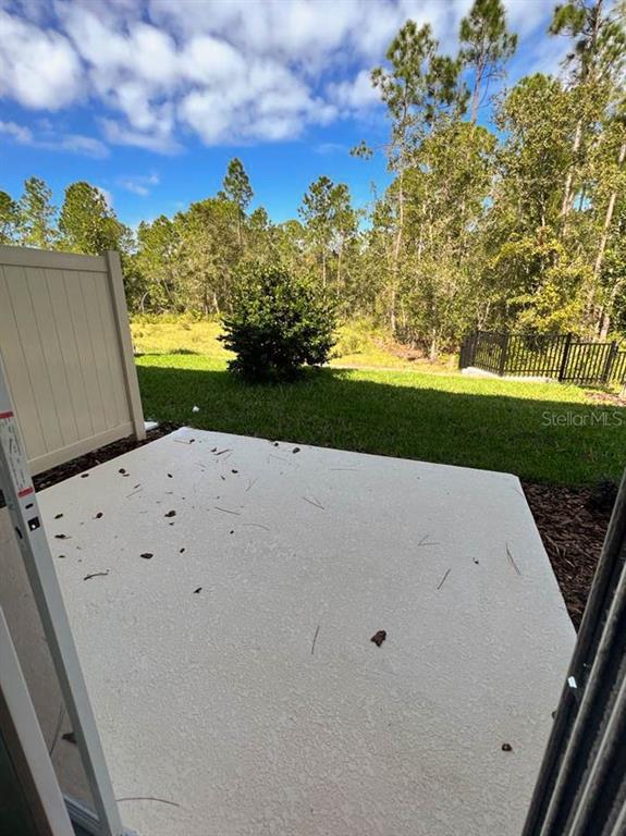 A concrete patio overlooks a grassy backyard with trees and a black metal fence — 3639 DAVENPORT CREEK COURT, KISSIMMEE, FL