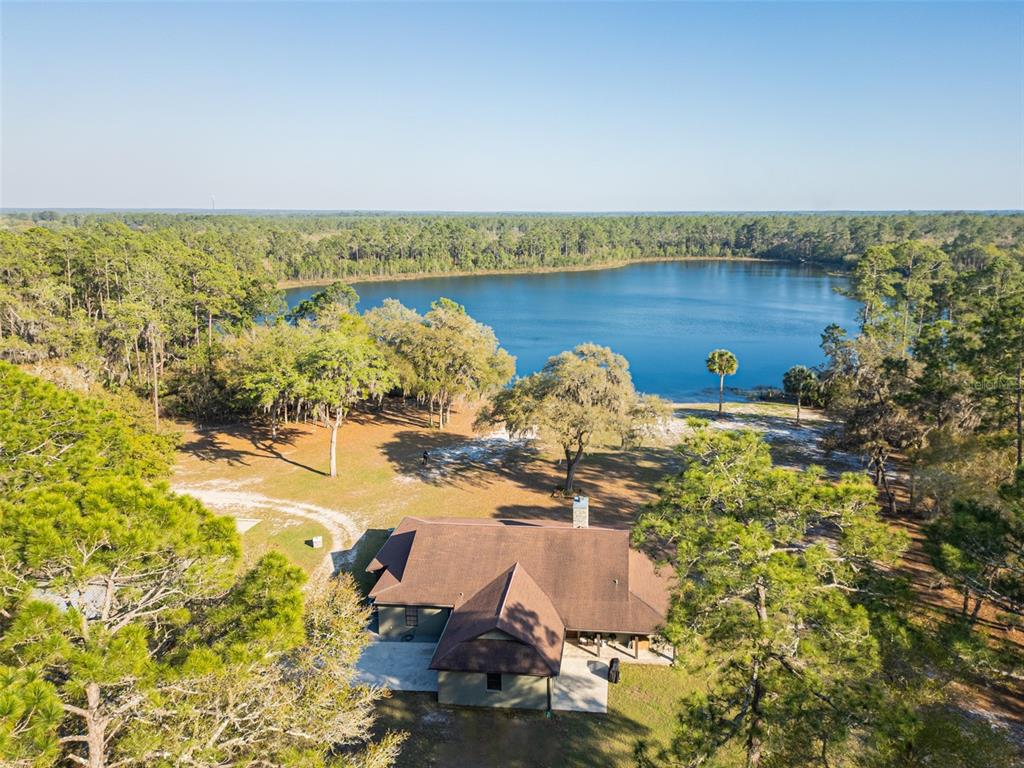 An aerial view shows a house with a brown roof situated near a large lake — 8600 NE 147TH AVENUE ROAD, SILVER SPRINGS, FL