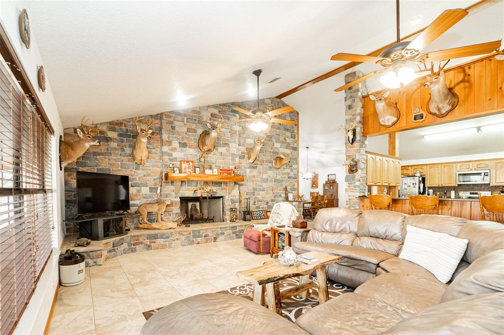 A living room features a stone fireplace, taxidermy mounts, tile flooring, and a leather sectional — 8600 NE 147TH AVENUE ROAD, SILVER SPRINGS, FL