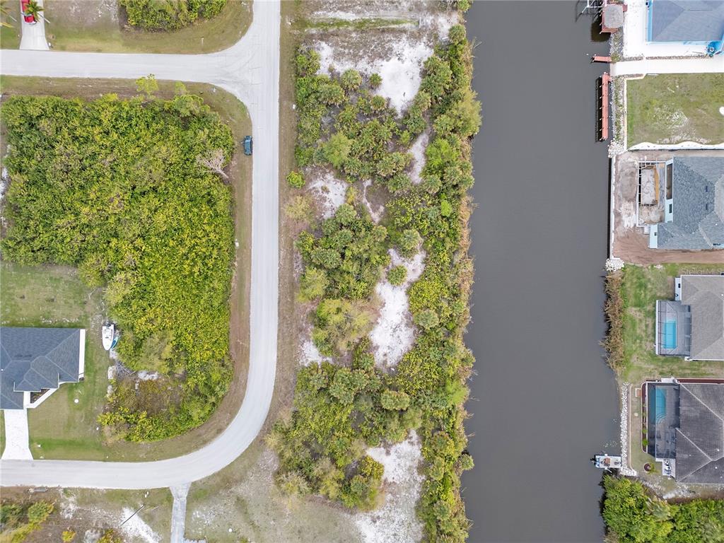 An aerial view shows a vacant, wooded lot situated between a residential street and a canal — 14246 FORT WORTH CIRCLE, PORT CHARLOTTE, FL