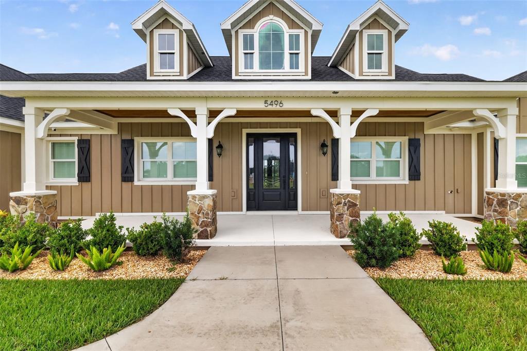 A tan house exterior features a covered porch with stone columns and three roof dormers — 5496 NANTAHALA LANE, LADY LAKE, FL