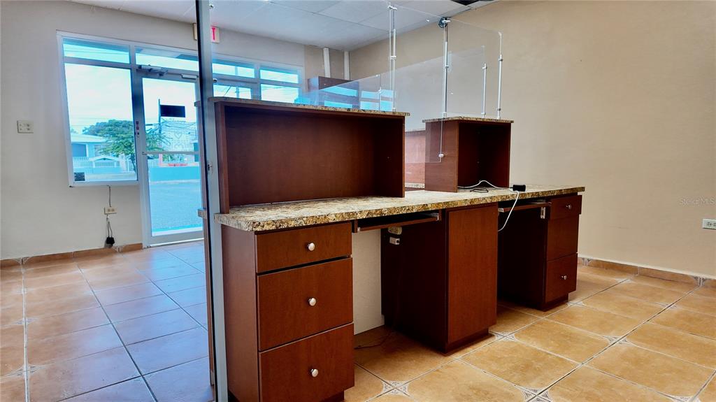 An office reception area features two wooden desks with granite countertops and glass partitions — 115 C. MARGINAL, RINCON, PR