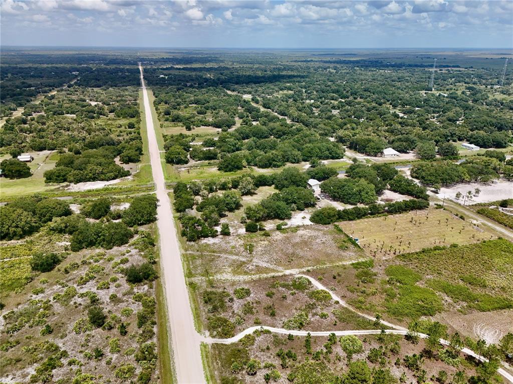 An aerial view shows a long, straight dirt road cutting through a rural, wooded landscape — 18277 NW 304TH STREET, OKEECHOBEE, FL