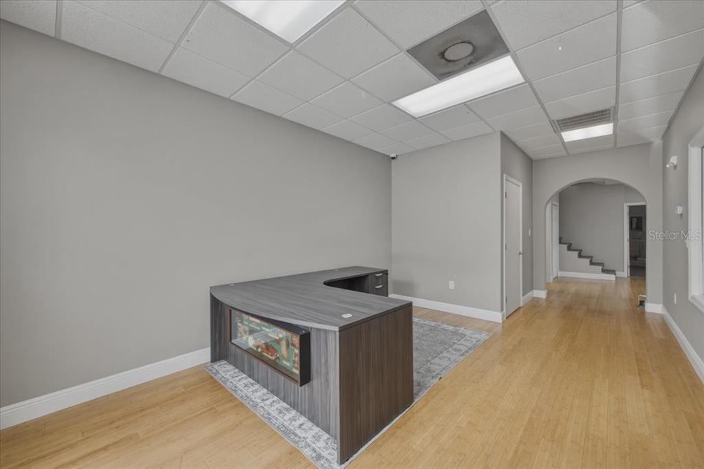 An office space features a wood-grain L-shaped desk on a rug with light-colored walls — 1882 PORTER LAKE DRIVE UNIT 106, SARASOTA, FL
