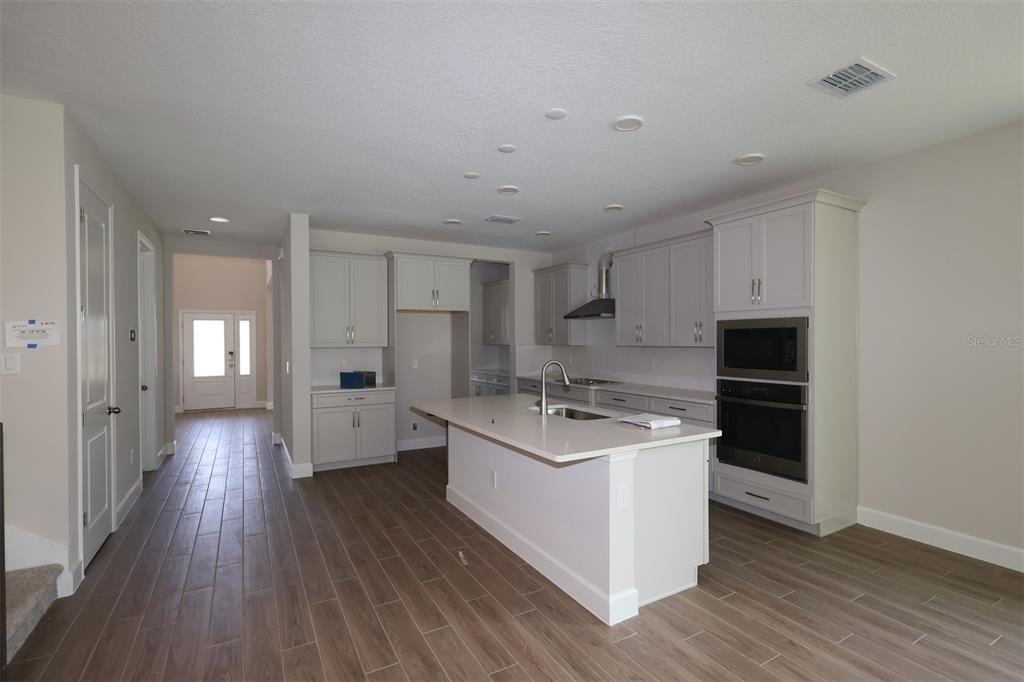 A modern kitchen features light gray cabinetry, a central island, and wood-look tile flooring — 1284 HYDE STREET, ST CLOUD, FL