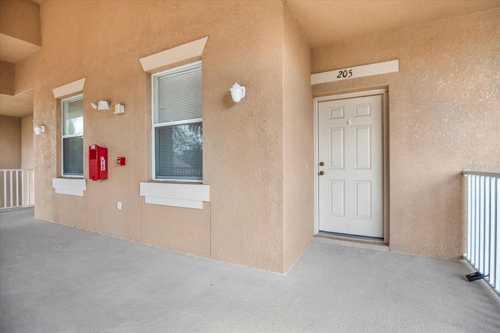 An exterior view of a building hallway featuring a white door labeled 205 — 1003 FAIRWAYCOVE LANE UNIT 205, BRADENTON, FL