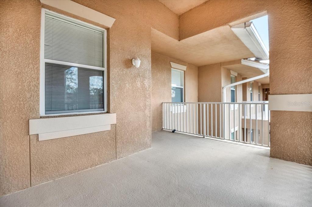 A covered balcony with beige stucco walls, a white metal railing, and two windows — 1003 FAIRWAYCOVE LANE UNIT 205, BRADENTON, FL