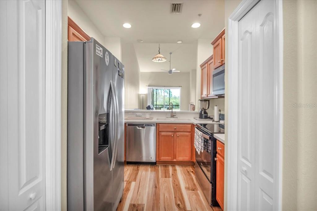 A galley kitchen features stainless steel appliances, wood cabinets, and light-colored wood flooring — 1003 FAIRWAYCOVE LANE UNIT 205, BRADENTON, FL