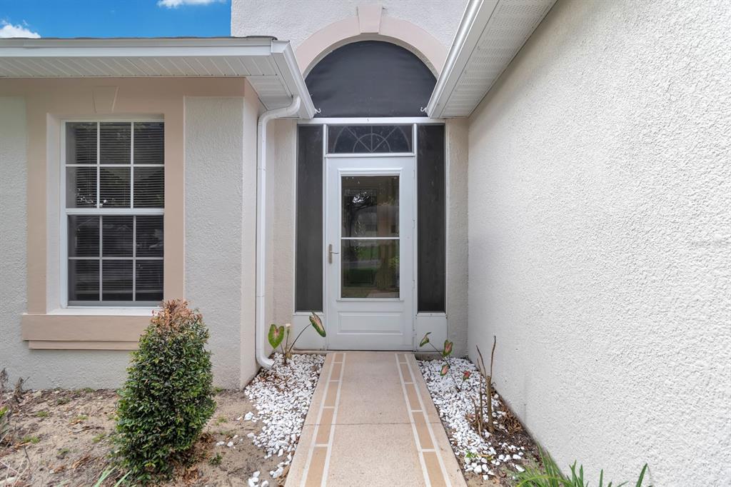 A white front door with a storm door is centered under an arched entryway — 4390 SAMBOURNE STREET, CLERMONT, FL