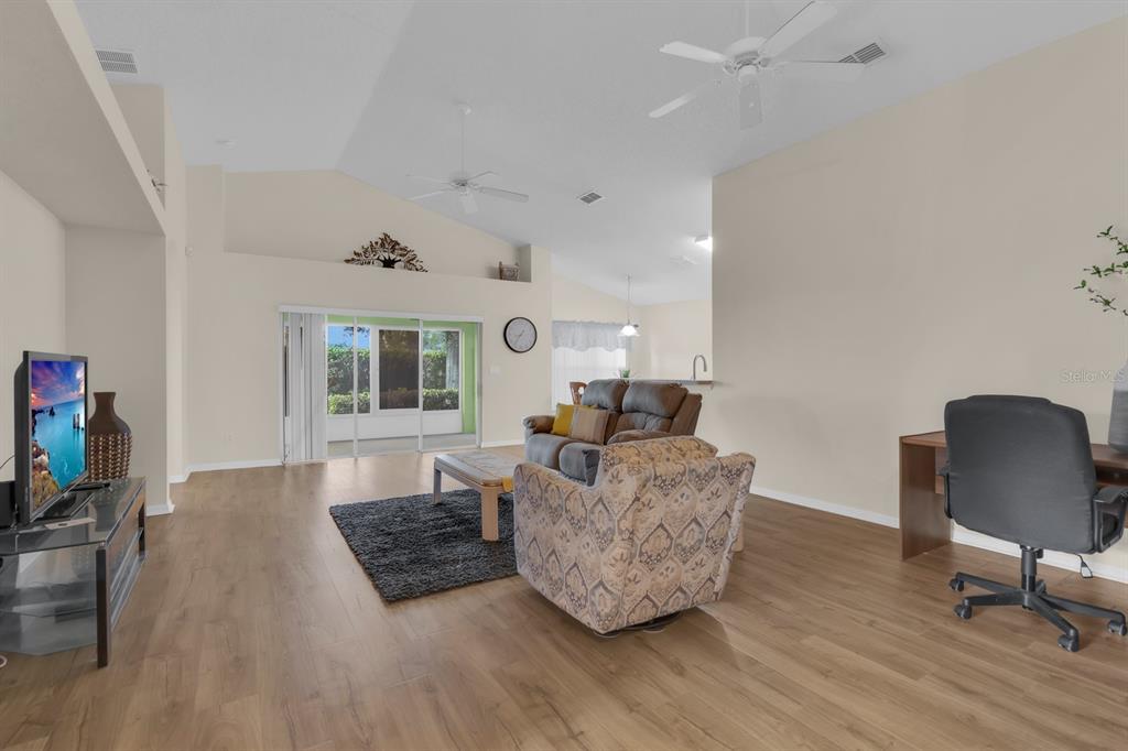 A living room features wood-look flooring, vaulted ceilings, a sliding glass door, and furniture — 4390 SAMBOURNE STREET, CLERMONT, FL