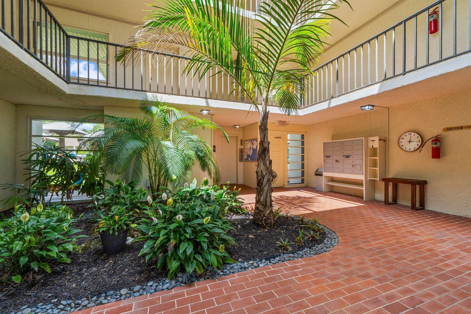 An open-air courtyard features a central palm tree, lush plants, brick flooring, and mailboxes — 1800 SE Saint Lucie Boulevard # 203, Stuart FL 34996, STUART, FL