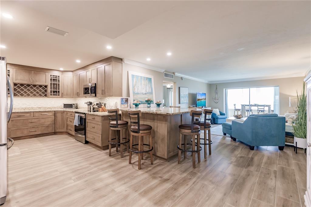 An open-concept kitchen with wood cabinets and a large island overlooks a living area — 1200 E PEPPERTREE LANE UNIT 602, SARASOTA, FL