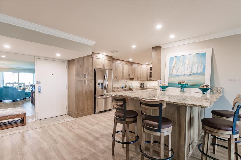 A kitchen features light wood cabinets, granite countertops, a large island with barstools, and stainless appliances — 1200 E PEPPERTREE LANE UNIT 602, SARASOTA, FL
