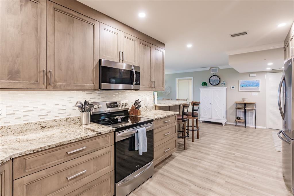 A kitchen features light wood cabinets, granite countertops, stainless steel appliances, and wood-look flooring — 1200 E PEPPERTREE LANE UNIT 602, SARASOTA, FL
