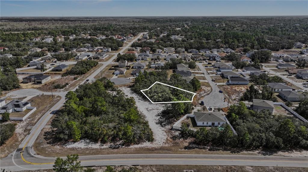 An aerial view shows a vacant, wooded residential lot outlined in white within a neighborhood — 611 AMAZON COURT, POINCIANA, FL
